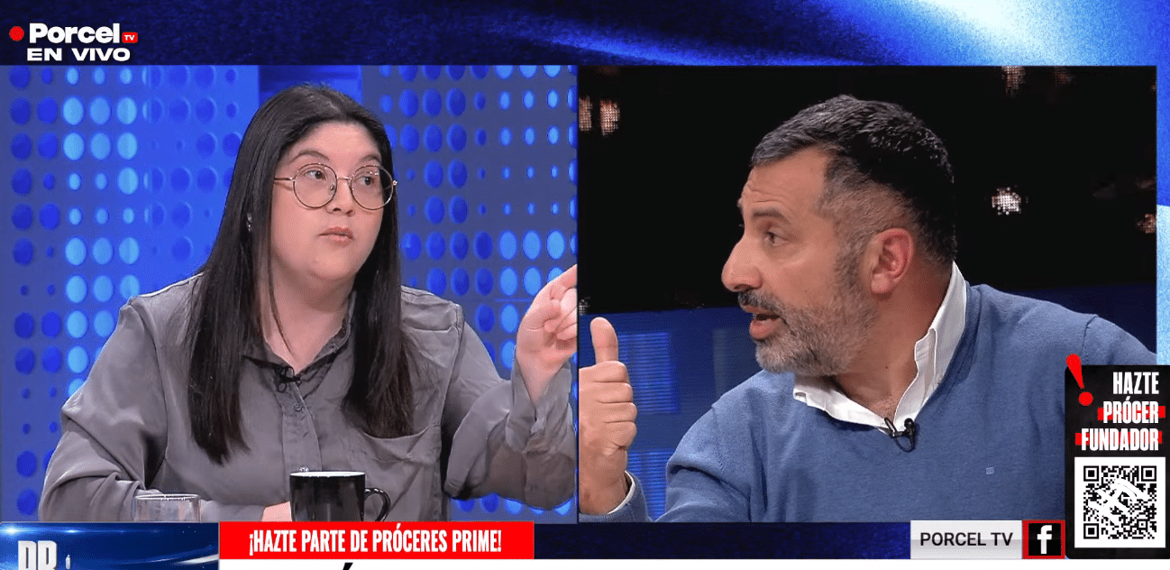 Pantalla dividida de un programa de televisión con una mujer de lentes y cabello oscuro gesticulando y un hombre de barba y suéter azul levantando el pulgar, en un estudio con fondo azul.