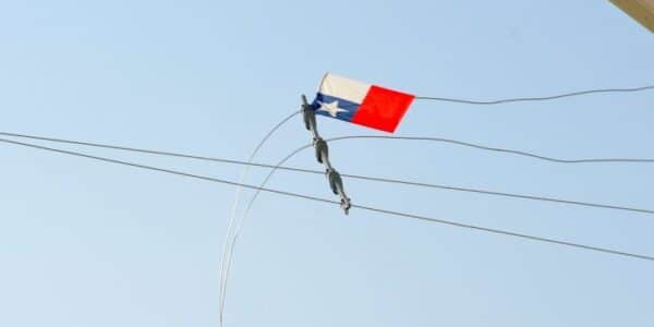 Un volantín con cola queda atrapado entre cables de tendido eléctrico contra un cielo despejado, mostrando el riesgo de elevarlo cerca de las líneas.