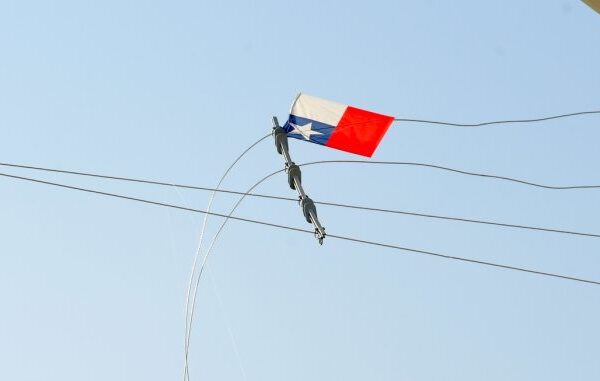 Un volantín con cola queda atrapado entre cables de tendido eléctrico contra un cielo despejado, mostrando el riesgo de elevarlo cerca de las líneas.