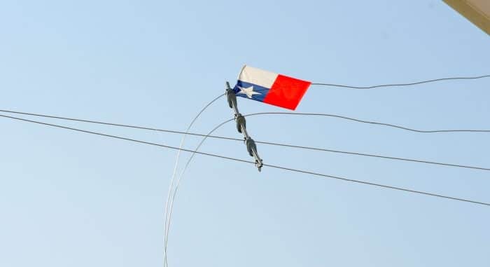 Un volantín con cola queda atrapado entre cables de tendido eléctrico contra un cielo despejado, mostrando el riesgo de elevarlo cerca de las líneas.