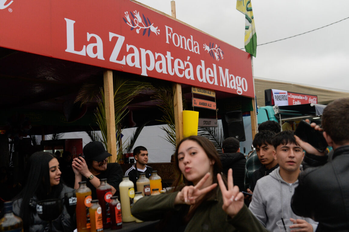 Letrero rojo de la fonda La Zapateá del Mago junto a asistentes en Fiestas Patrias 2026