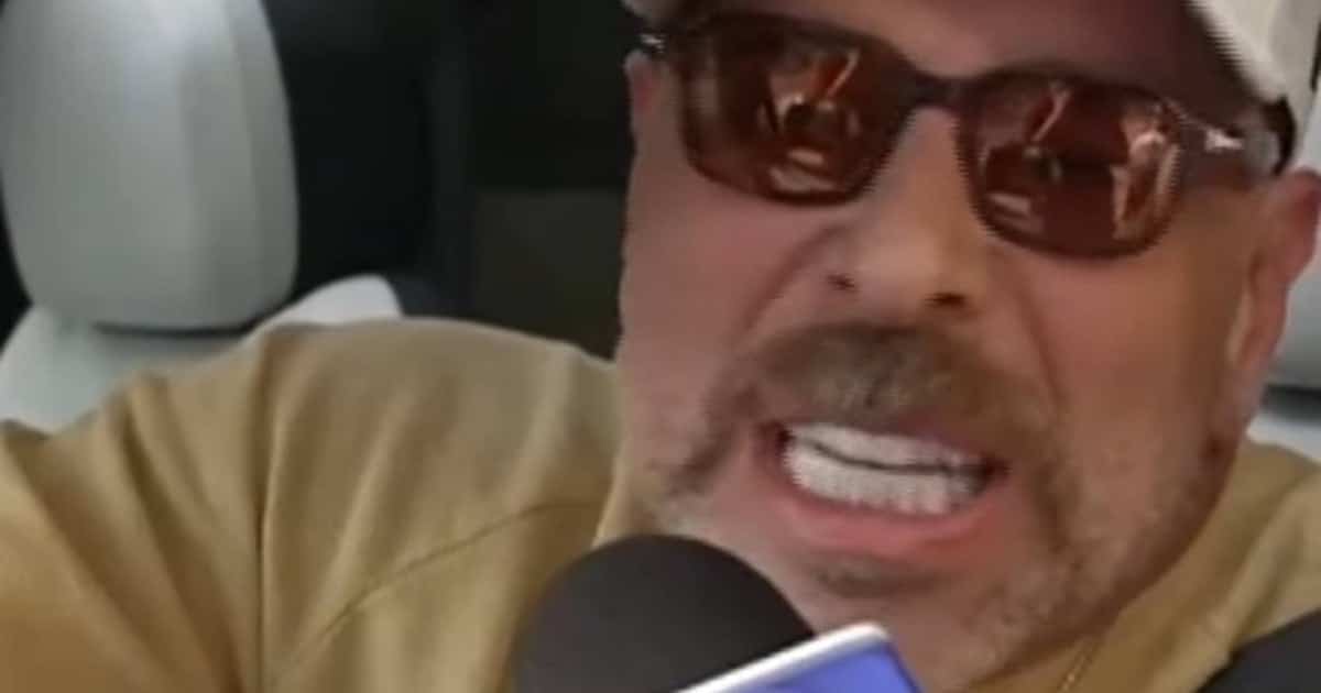 Primer plano de un hombre con gorra clara y lentes oscuros, hablando con expresión intensa frente a un micrófono.