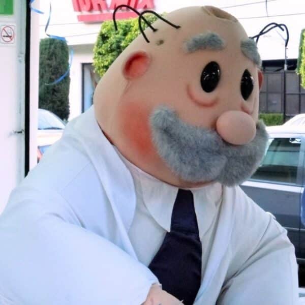 Una persona disfrazada de Dr. Simi, con bata blanca y corbata oscura, aparece en la entrada de un local, con autos y personas al fondo.