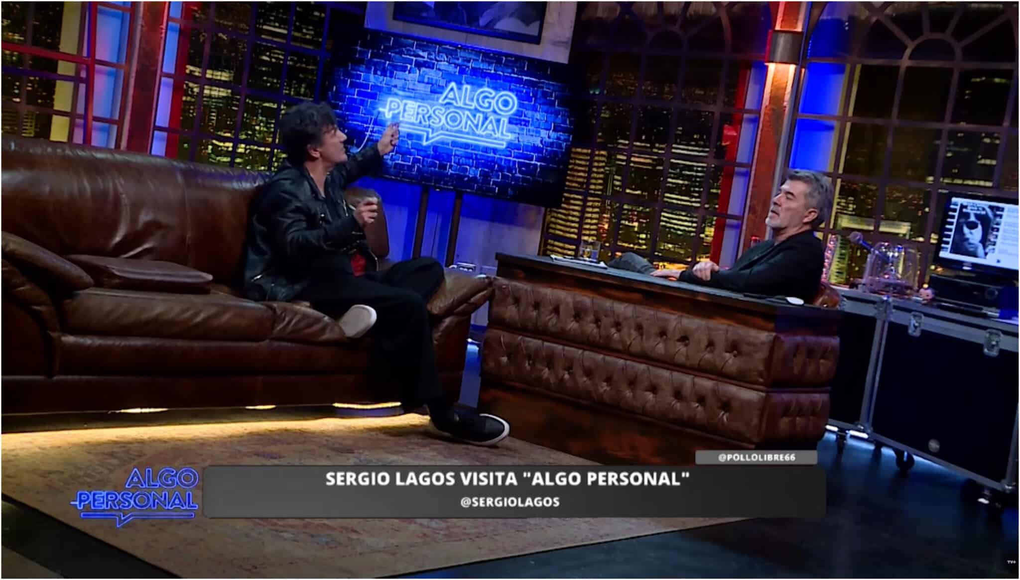 Dos hombres conversan en un estudio de televisión con sillones de cuero café; uno gesticula sentado en un sofá y el otro escucha tras un escritorio, bajo un letrero luminoso que dice Algo Personal.