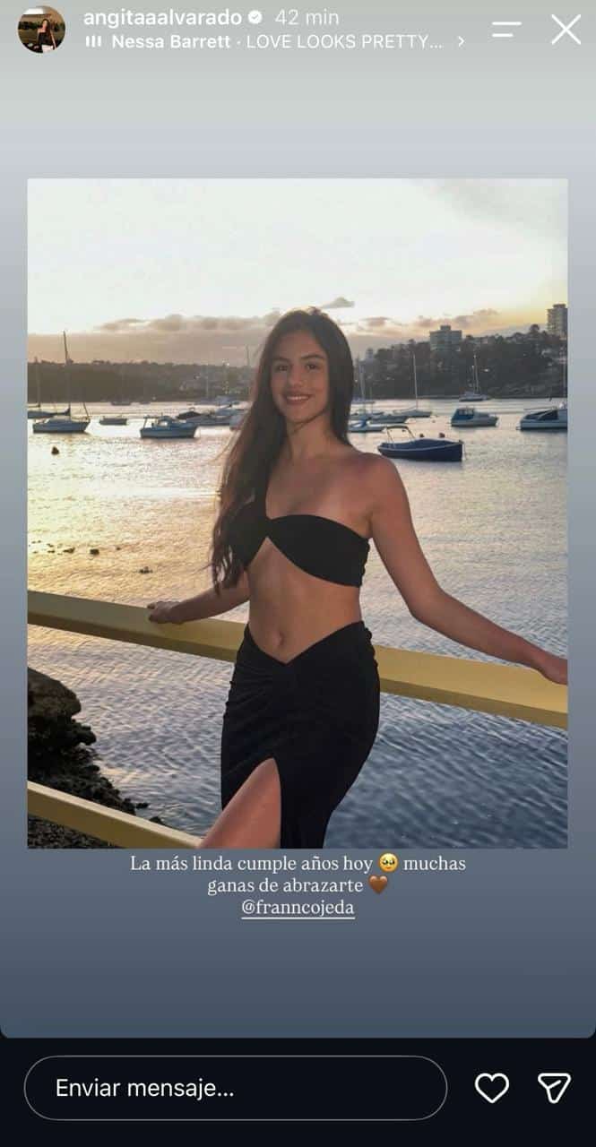 Una mujer con top negro y falda posa junto a una baranda, con botes y agua al fondo. La imagen aparece en una historia de redes sociales.