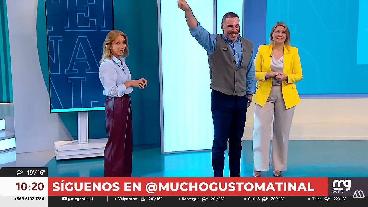 Un hombre al centro levanta un brazo junto a dos mujeres en un estudio de televisión. Una viste chaqueta amarilla y la otra blusa celeste; al pie aparece una franja roja con texto.